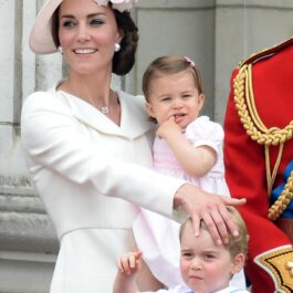 Kate Middleton poartă o rochie albă cu mâneci, cambrată și o pălărie masivă de culoare roz pal