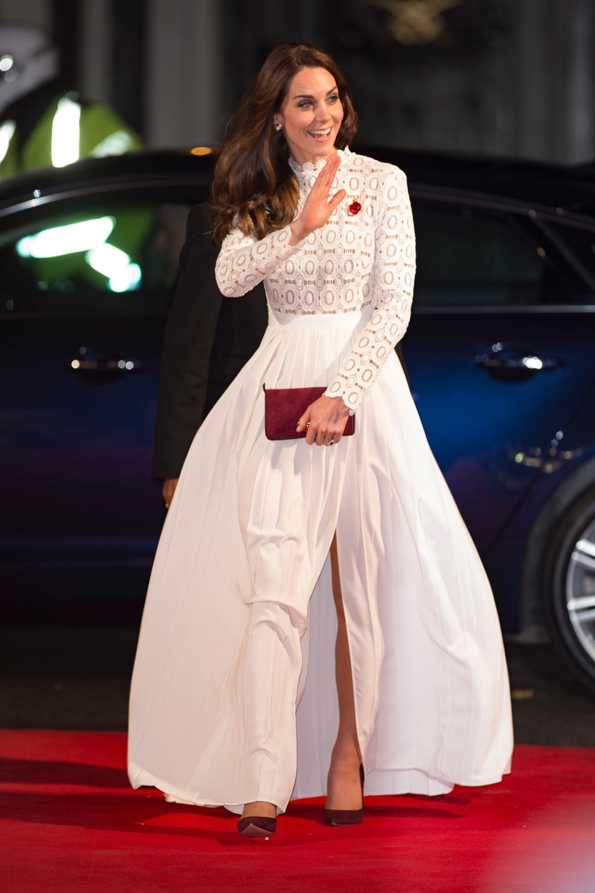 Kate poartă o rochie de culoare albă cu aplicații de dantelă în partea de sus și o broșă de culoare roșie