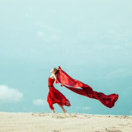 Fată frumoasă îmbrăcată în roșu stă în deșert