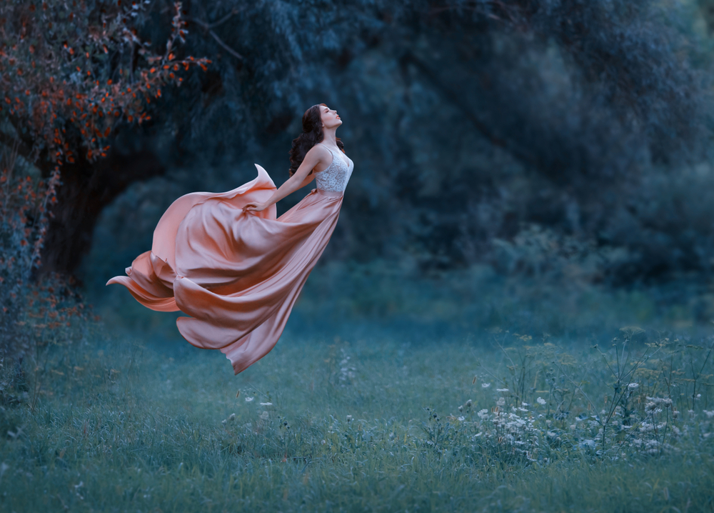 Fată frumoasă îmbrăcată într-o rochie lungă stă într-o pădure