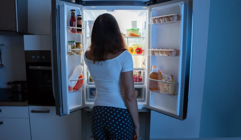 O femeie frumoasă care mănâncă în timpul nopții din frigiderul său