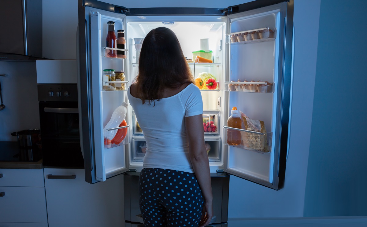 O femeie frumoasă care mănâncă în timpul nopții din frigiderul său