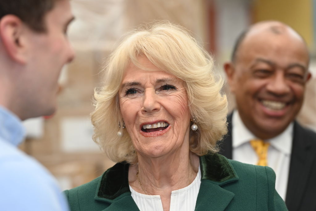 Regina Camilla, la un evenimenr, cu zâmbetul pe buze, într-un costum verde, în timp ce discută cu gazdele