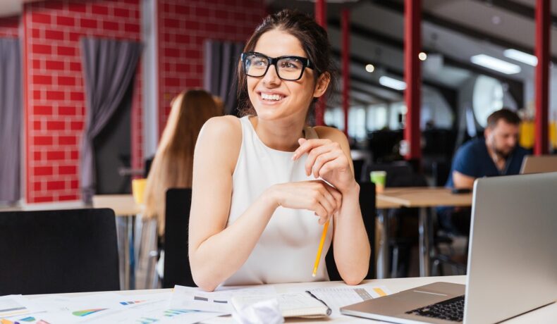 O femeie frumoasă care poartă ochelari și stă la birou pentru a putea ilustra câteva obiceiuri simple care să te ajute să ai o zi productivă