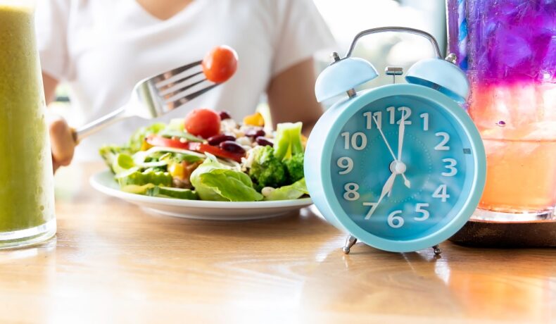 Un ceas care se află în fața unei farfurii cu salată pentru a ilustra postul intermitent ca metodă de slăbit