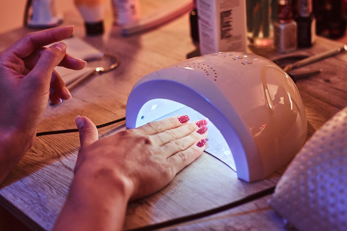 O femeie frumoasă care îți ține mâinile la o lampă UV pentru unghii