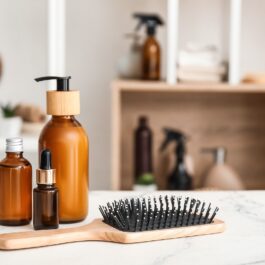 Mai multe produse de îngrijire a părului printre care și un ser de hidratare și o perie de păr din bambus, aflate pe un blat de marmură dintr-o baie de culoare albă