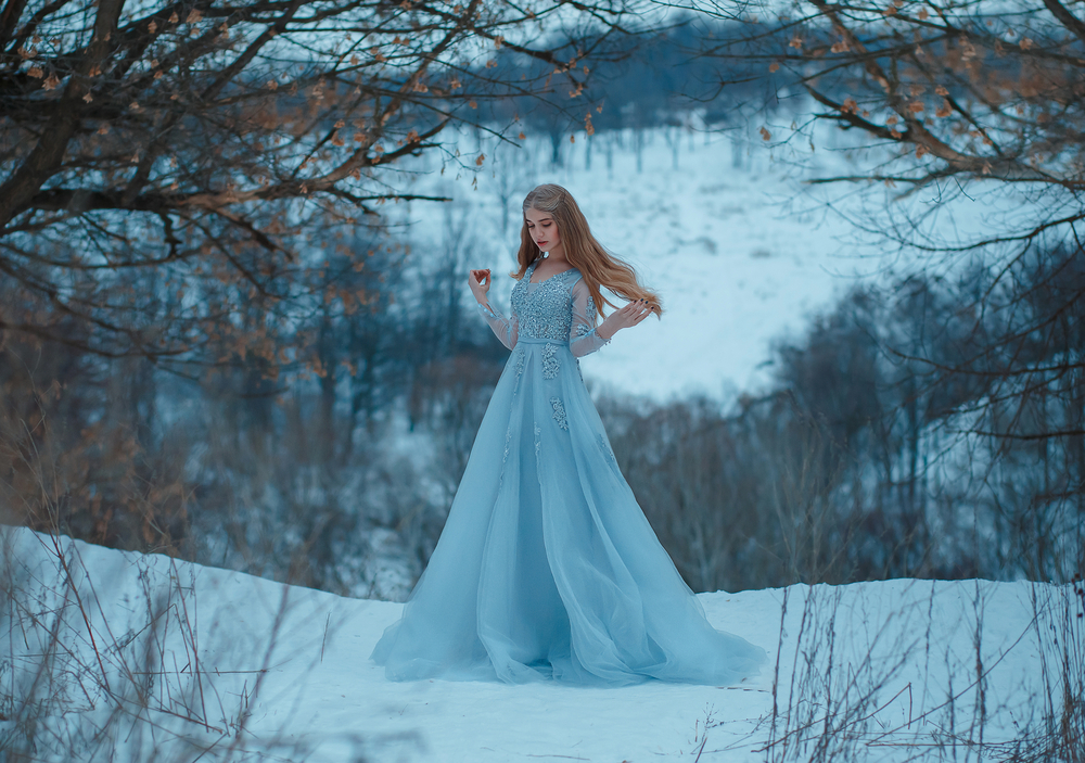 Fată frumoasă îmbrăcată într-o rochie lungă, albă stă pe zăpadă