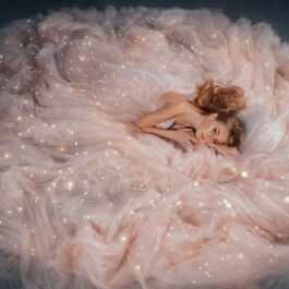 O fată frumoasă, tânără, îmbrăcată într-o rochie roz pal, voluminoasă cu multe cristale strălucitoare