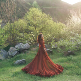 Fată frumoasă brunetă cu rochie lungă vișinie stă într-o pădure
