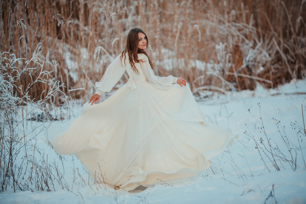Fată frumoasă îmbrăcată într-o rochie albă merge prin zăpadă