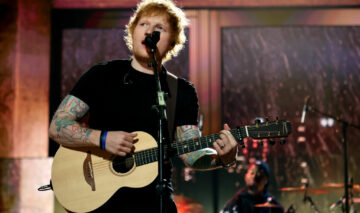 Ed Sheeran, pe scenă, cu chitara în mână, în timp ce interpretează o melodie