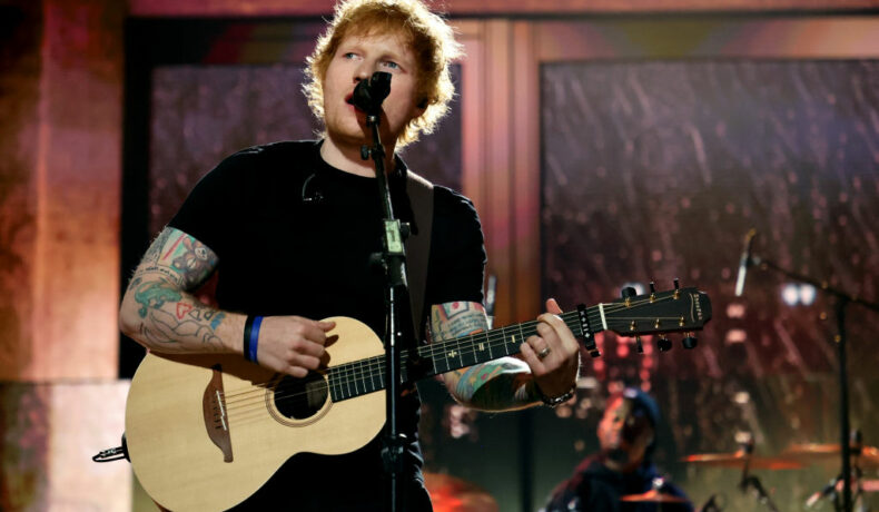 Ed Sheeran, pe scenă, cu chitara în mână, în timp ce interpretează o melodie