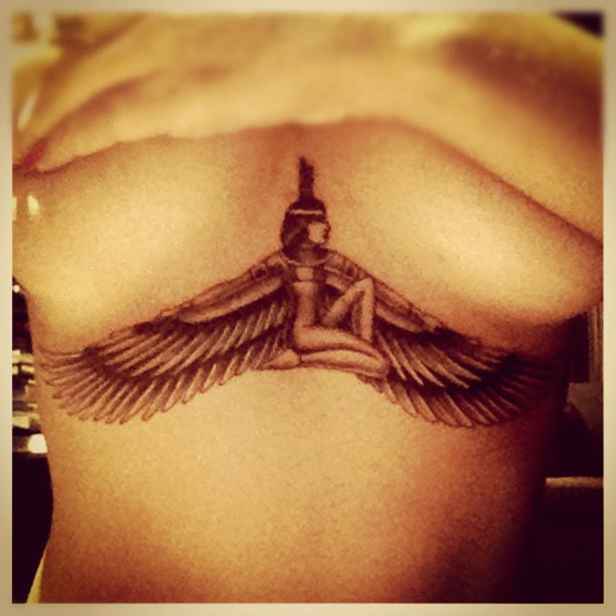 Rihanna, dezbrăcată în partea de sus, cu mâinile pe bust, în timp ce își arată tatuajul