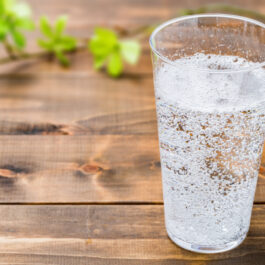 Un pahar cu apă minerală, transparent, pe un blat din lemn