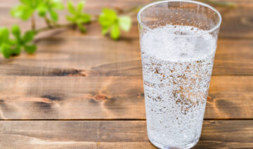 Un pahar cu apă minerală, transparent, pe un blat din lemn