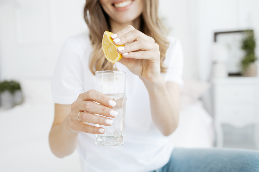 O femeie care stoarce o felie de lămâie într-un pahar cu apă