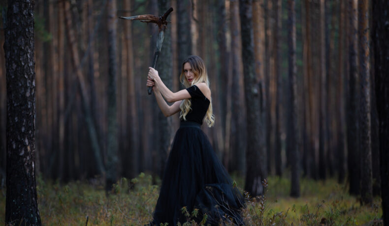 Fată frumoasă îmbrăcată într-o rochie neagră stă într-o pădure