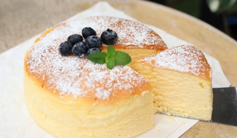 Cheesecake japonez porționat și decorat cu zahăr pudră, afine și frunze de mentă