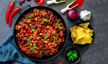 Chili vegan în tigaie, alături de un bol cu tacos și condimente