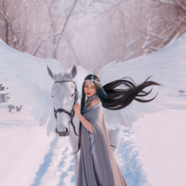 Fată frumoasă îmbrăcată într-o rochie lungă stă lângă un cal alb