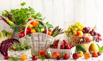 O masă pe care se află un coș plin cu fructe și legume ieftine pe care le găsești în sezonul de primăvară