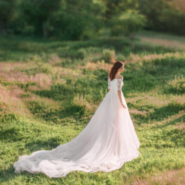 Fată frumoasă îmbrăcată într-o rochie lungă albă stă într-o pădure