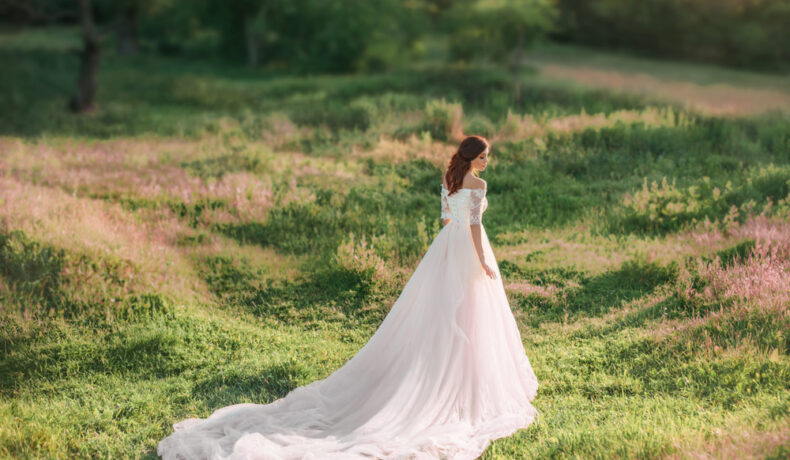 Fată frumoasă îmbrăcată într-o rochie lungă albă stă într-o pădure