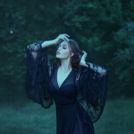 Fată frumoasă îmbrăcată într-o rochie neagră stă într-o pădure