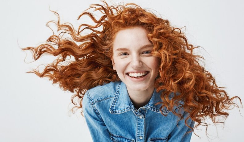 O femeie frumoasă cu părul creț roșcat pentru a ilustra cum să ai grijp de acest tip de păr