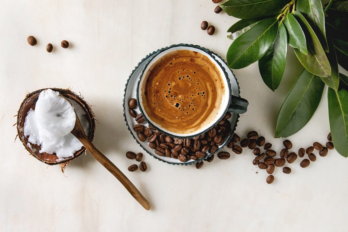 O ceașcă plină de cafea alături de o linguriță cu ulei de cocos