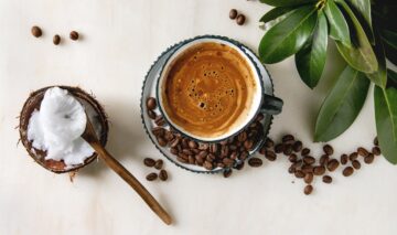 O ceașcă plină de cafea alături de o linguriță cu ulei de cocos