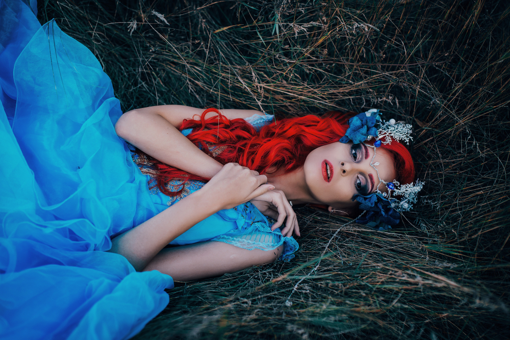 Fată frumoasă într-o rochie albastră lungă, stă pe iarbă întinsă