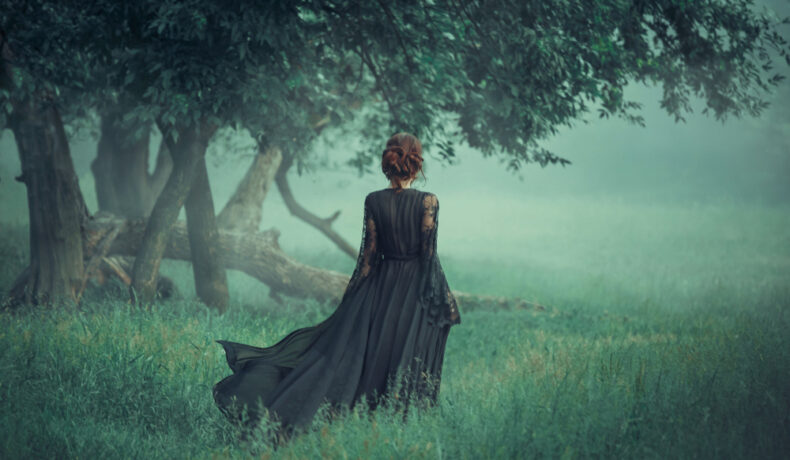 Fată frumoasă îmbrăcată într-o rochie lungă neagră merge prin pădure