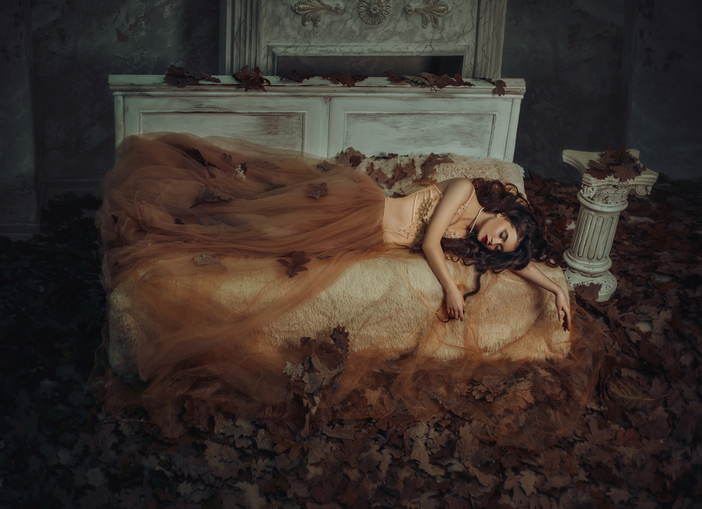 Fată frumoasă îmbrăcată într-o rochie lungă stă întinsă în pat