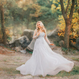 Fată frumoasă îmbrăcată într-o rochie lungă, albă stă într-o pădure