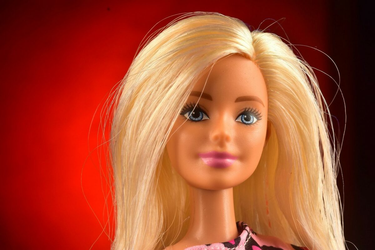 O păpușă Barbie, blondă, cu ochii verzi, fotografiată pe un fundal roșu