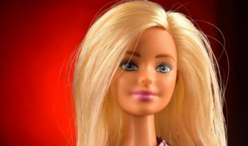 O păpușă Barbie, blondă, cu ochii verzi, fotografiată pe un fundal roșu