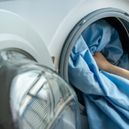 O femeie care bagă cearșafurile la spălat în mașina de rufe