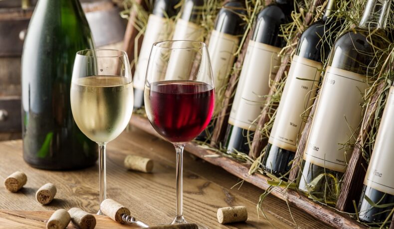 Mai multe sticle de vin alături de două pahare, unul cu vin alb și unul cu vin roșu