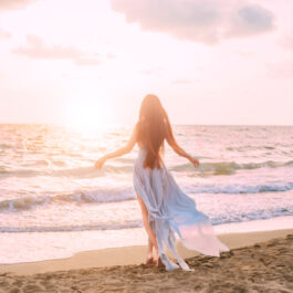 Fată frumoasă îmbrăcată într-o rochie de voal stă cu fața îndreptată către mare