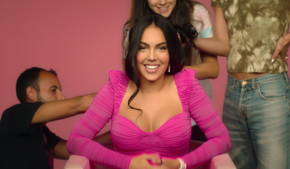 Georgina Rodriguez, fotografiată pe un fundal roz, în timp ce este coafată și aranjată de echipa ei de stiliști