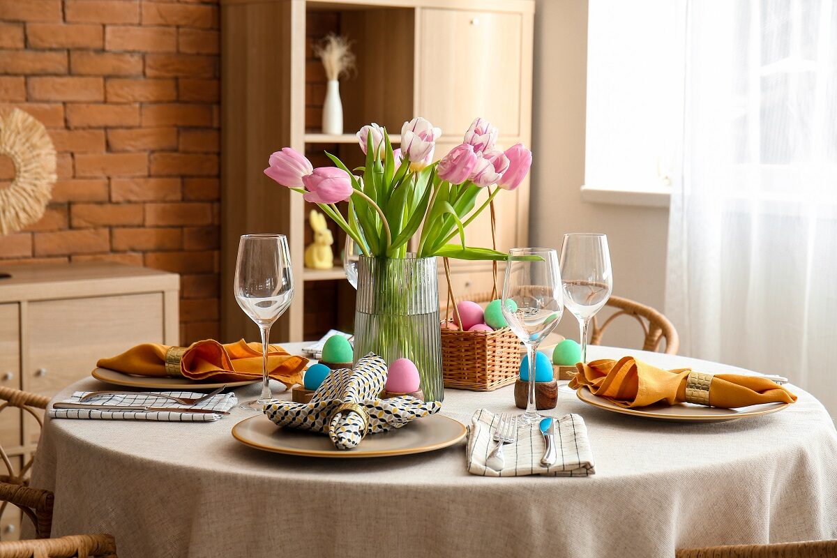 Masa de Paște 2023 aranjată cu farfurii și o vază frumoasă cu lalele roz