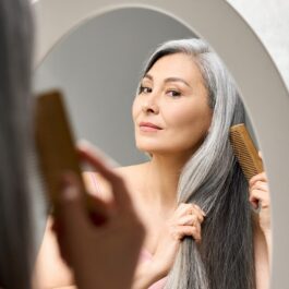 O femeie frumoasă care își piaptănă părul grizonat în timp ce se privește în oglindă