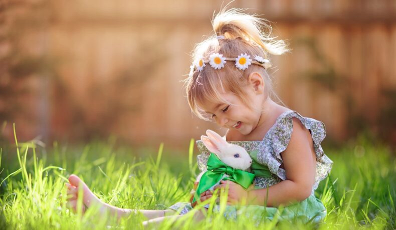O fetiță frumoasă care ține în brațe un iepuraș alb pentru a ilustra povestea Iepurașului de Paște