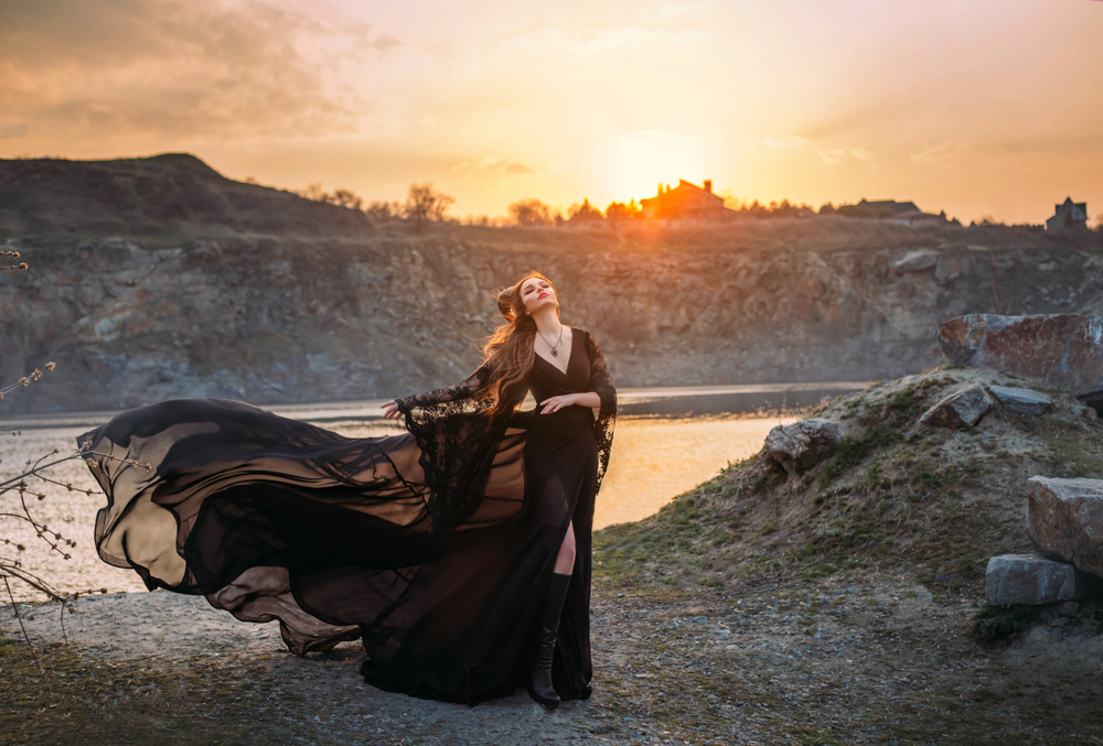 Fată frumoasă îmbrăcată într-o rochie lungă, neagră, stă lângă un lac