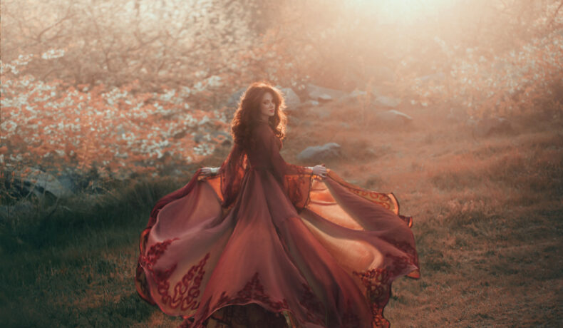 Fată frumoasă îmbrăcată într-o rochie lungă de voal stă într-o pădure