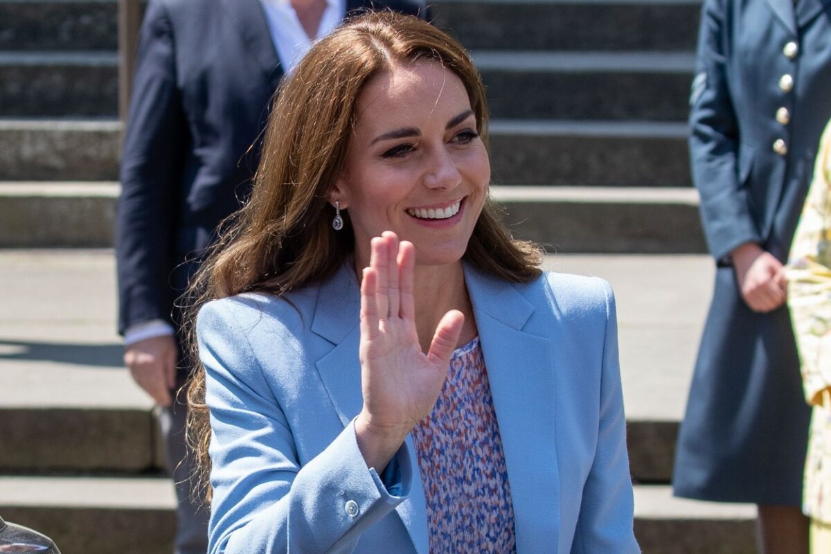 Kate Middleton le face cu mâna admiratorilor, îmbrăcată într-un sacou albastru și o bluză cu detalii florale