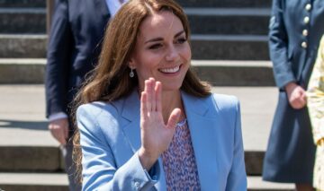 Kate Middleton le face cu mâna admiratorilor, îmbrăcată într-un sacou albastru și o bluză cu detalii florale