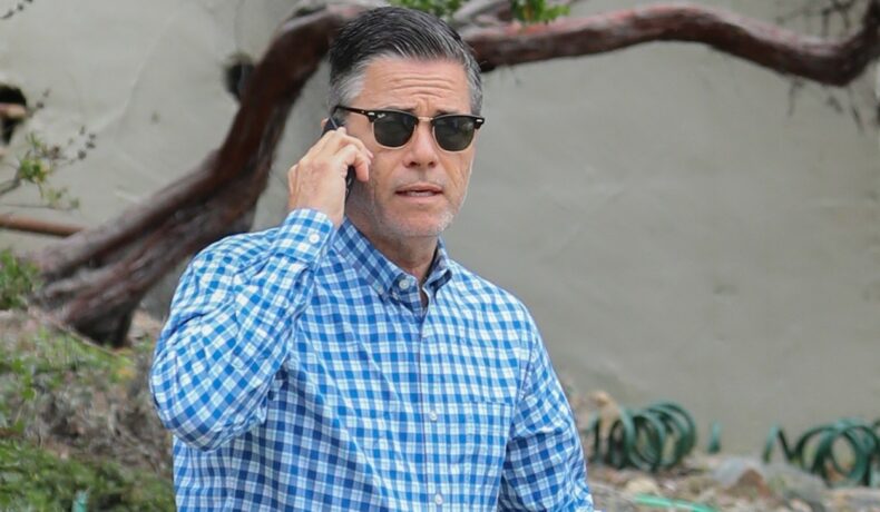 Scriitorul J.R Moehringer, fotografiat în timp ce vorbește la telefon și e îmbrăcat într-o cămașă albastră și poartă ochelari de soare